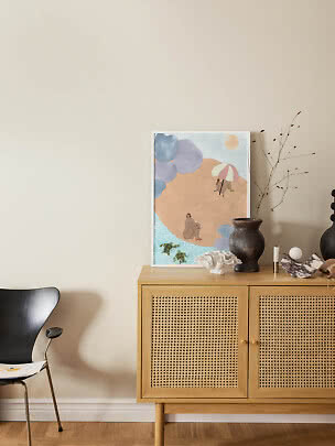 Ingelijste abstracte strandposter op eiken dressoir met vaas, koraal en kaars tegen beige muur
