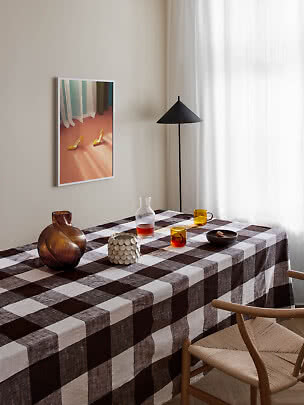 Dining table with brown checkered tablecloth, glasses, vase and chair in a bright room