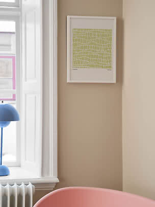 White-framed graphic print with green pattern on a beige wall beside a window