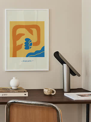 Ingelijste abstracte poster met gele, oranje en blauwe vormen boven een bureau