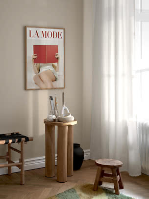 Coin lumineux avec table d'appoint ronde en bois, petit tabouret et affiche La Mode encadrée