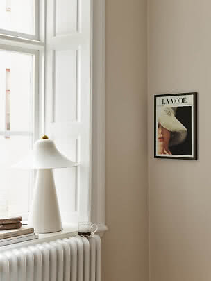 White table lamp on windowsill by radiator, with books, cup and framed poster on beige wall