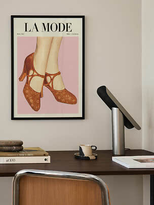 Framed fashion poster showing illustrated legs in brown shoes above a desk