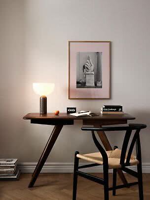 Bureau en bois foncé avec lampe allumée, livres, carnet ouvert et chaise noire sous une œuvre encadrée