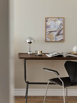 Bureau minimaliste avec lampe chromée, tasse, livre ouvert et art abstrait encadré au mur