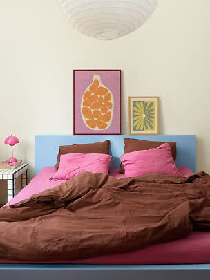 Chambre colorée avec lit bleu clair, linge de lit rose, couette marron, lampe rose et cadres