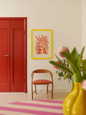 Colorful interior with red door, wooden chair, yellow vase with tulips, and wall art.