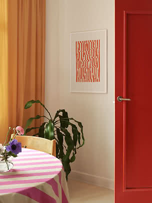 Dining corner with pink striped tablecloth, flowers, green plant, orange curtain and red door