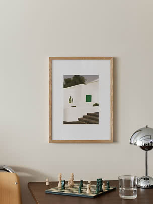 Framed photo print of a white building with green shutters and stone steps on a beige wall
