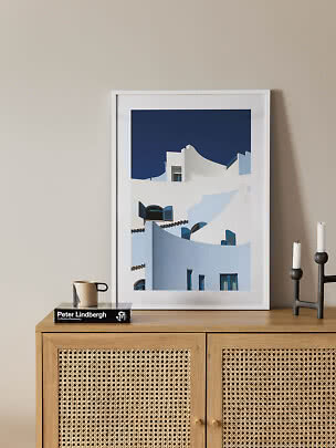 Framed print of white buildings with blue shutters on a wooden sideboard