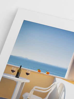 Angled view of terrace with white table, chair, wine bottle, two glasses of red wine, and sea view