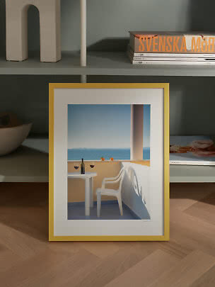Framed print with yellow frame showing a balcony with chair, table, wine and sea view