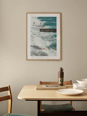 Framed ocean photo with surfers and waves hanging above a dining table