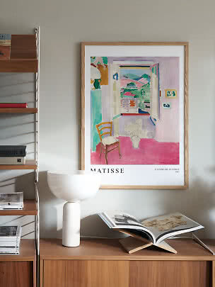 Gerahmtes Matisse-Poster an der Wand über Holzschrank mit weißer Lampe und offenem Buch