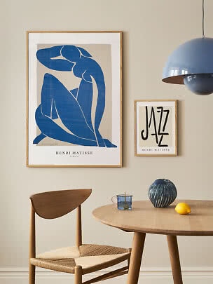 Spiseplads med stor blå Matisse-plakat, lille Jazz-plakat, træstol, rundt bord, vase og citron