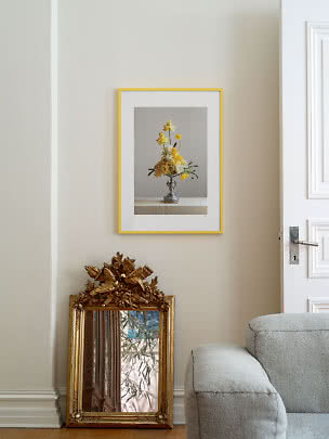 Guldramme med blomsterplakat på beige væg over et ornamenteret guldspejl.