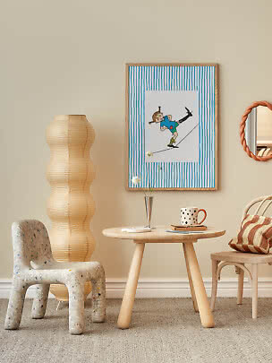 Angolo accogliente con poster per bambini, tavolo in legno, lampada in carta e tazza a pois