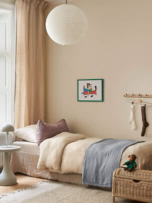Accogliente cameretta con letto singolo, lampada a sospensione in carta e baule intrecciato.