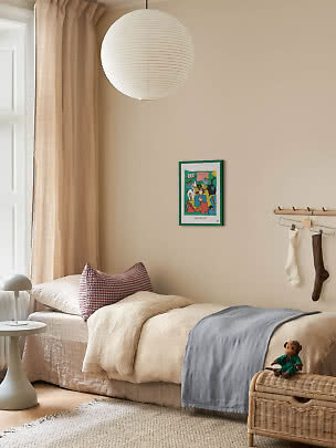 Accogliente cameretta con letto singolo, lampada in carta, tende beige e panca in vimini