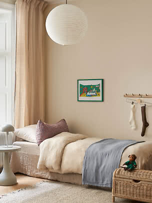 Hyggeligt børneværelse med enkeltseng, papirlampe, beige gardiner og kurvekiste