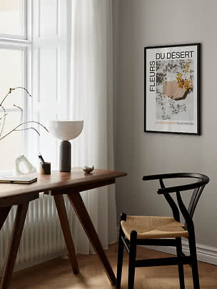Indrammet kunstplakat på beige væg over træbord ved vindue i lys, minimalistisk stue