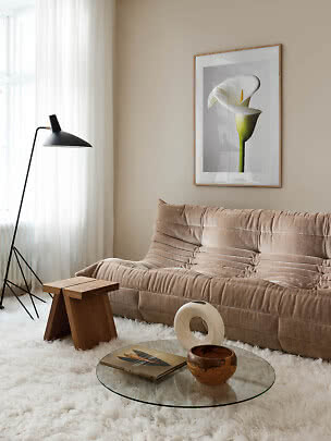 Moderne stue med beige sofa, sort gulvlampe, glasbord og blomsterplakat på væggen