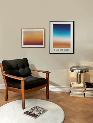 Rincón de salón con sillón negro de madera, dos pósteres coloridos y lámpara cromada