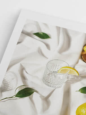 Verre texturé avec tranche de citron sur tissu blanc, entouré de feuilles vertes