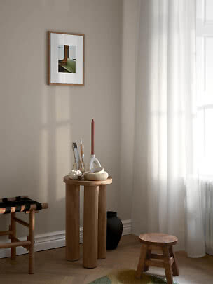 Gemütliche Ecke mit rundem Holztisch, Kerzenhalter, Hocker und gerahmtem Bild an beiger Wand