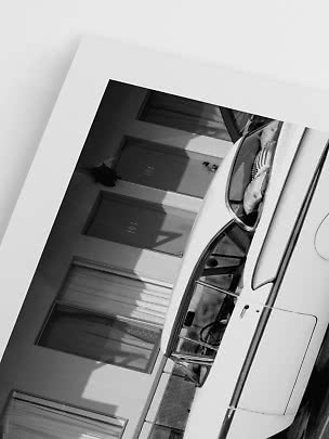 Foto en blanco y negro de un coche familiar blanco aparcado frente a habitaciones de motel.