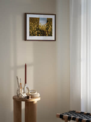 Lámina floral enmarcada en pared beige sobre una pequeña mesa de madera con vela y decoración