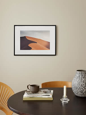 Indrammet fotokunst af sandklitter hænger over rundt bord med vase, lysestage og kop