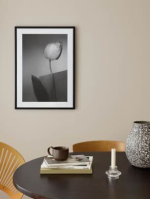 Sort indrammet sort-hvid plakat med tulipan på beige væg over rundt bord.