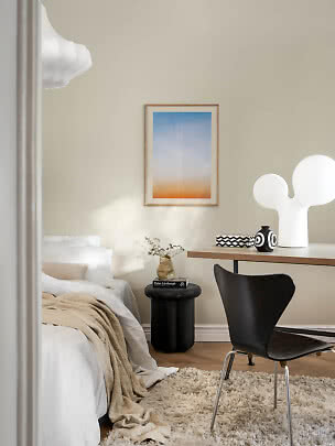 Lichte slaapkamer met bed, bureau, zwarte stoel, witte tafellamp en ingelijste kunst aan de muur