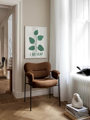 Brun polstret stol ved vindue med botanisk plakat på beige væg