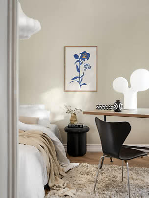 Cozy bedroom with desk, black chair, white table lamp, and floral poster on a beige wall
