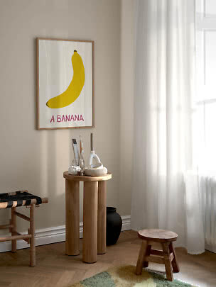 Inramad poster med gul banan på beige vägg i ett ljust rum