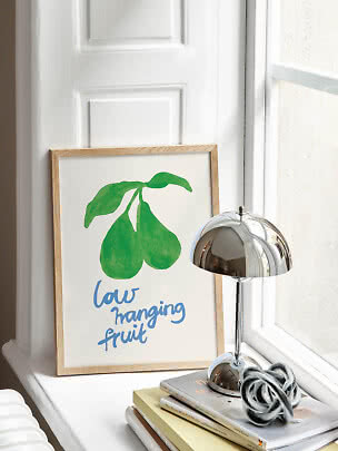Gerahmtes Poster mit grünem Birnenzweig und blauem Text auf einer Fensterbank neben Chromlampe