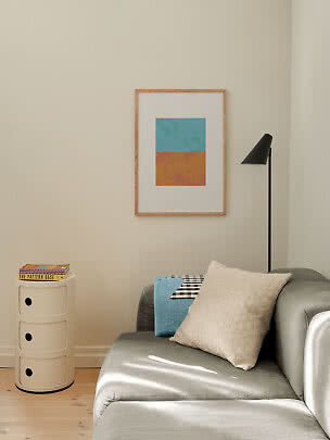 Stuehjørne med grå sofa, puder, sort gulvlampe og indrammet abstrakt kunst på væggen