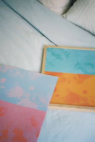 Due stampe artistiche colorate in azzurro pastello, rosa e arancione su un letto bianco