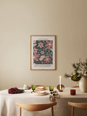 Poster floreale incorniciato sopra tavola apparecchiata con candela, bicchieri verdi e vaso con rami