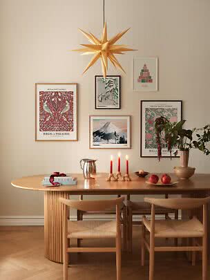 Cozy dining room with wooden table, chairs, star pendant lamp, framed prints, red candles and fruit
