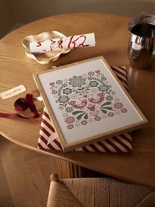 Gerahmter Folk-Art-Druck mit Blumen und Vögeln auf Holztisch mit Geschenkpapier und Band