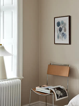 Framed tree illustration on beige wall above chair with leather back and magazines