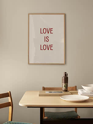 Indrammet plakat med teksten “LOVE IS LOVE” i rødt på hvid baggrund over et spisebord