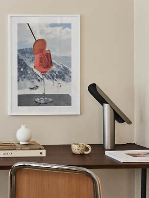 Bureau avec lampe noire et affiche encadrée d’un cocktail rose devant des montagnes enneigées