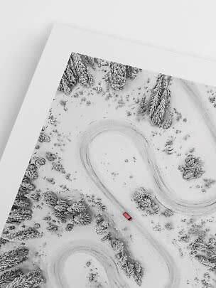 Foto aerea incorniciata di strada invernale tortuosa nel bosco innevato con auto rossa