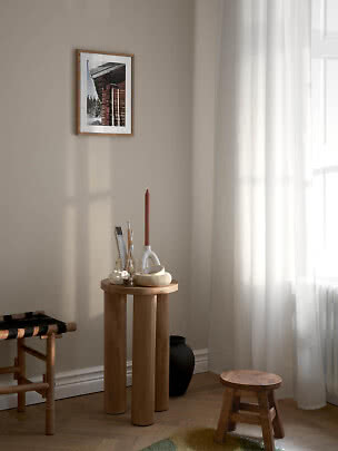 Helle Ecke mit Holzschemel, rundem Beistelltisch und gerahmtem Foto an beigefarbener Wand