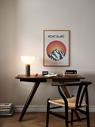 Skrivebord i mørkt træ med stol, bordlampe, bøger og Mont Blanc-plakat på væggen