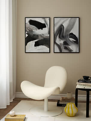 Two framed black-and-white abstract prints above a cream lounge chair in a calm modern room.